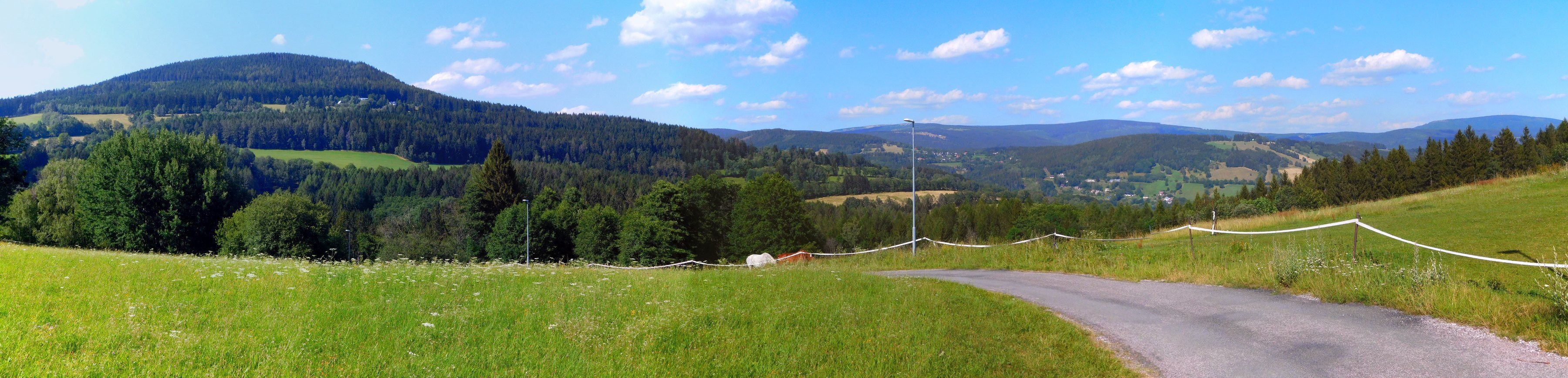 Letní panorama Krkonoš od Kněžic: vlevo zalesněný Žalý, uprostřed údolí s vesnicemi, vpravo na obzoru Černá hora